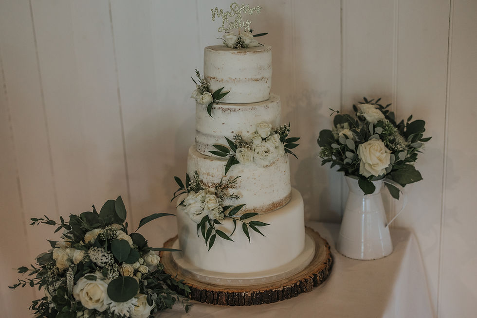 Three-tier rustic wedding cake with white flowers and greenery on wooden log base.