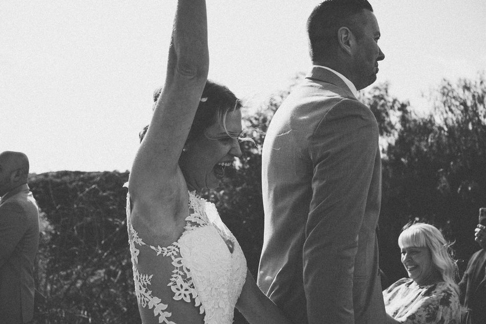 Bride raises her bouquet up and smiles as she walks down the aisle with her husband