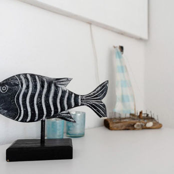 2 blau und türkis-weiße Holzfische auf Standfuß stehen auf einem Sideboard.