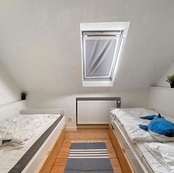 Blick in ein Schlafzimmer mit Dachschräge und Dachfenster. Zwei Einzelbetten stehen rechts und links an der Wand.