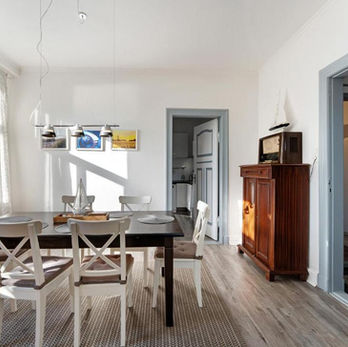 Esszimmer mit dunklem Holztisch und sechs Stühlen. die Fenster befinden sich gegenüber der Zimmertür, geradeaus geht es in die Küche.