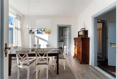Esszimmer mit dunklem Holztisch und sechs Stühlen. die Fenster befinden sich gegenüber der Zimmertür, geradeaus geht es in die Küche.
