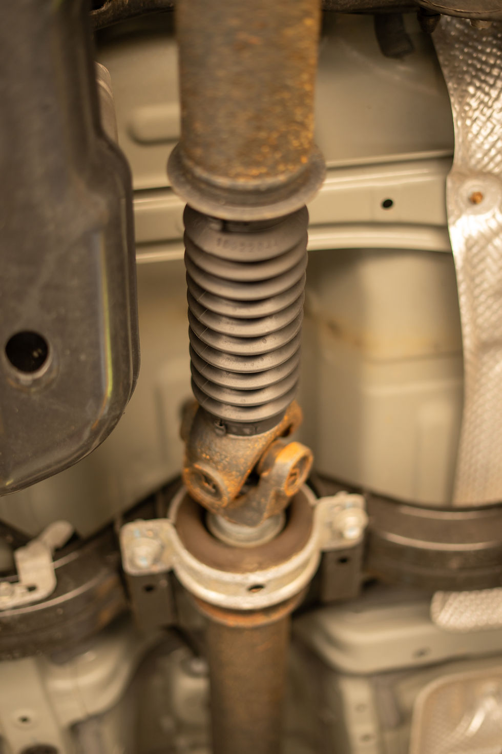 Black and rusty driveshaft on underside of vehicle.