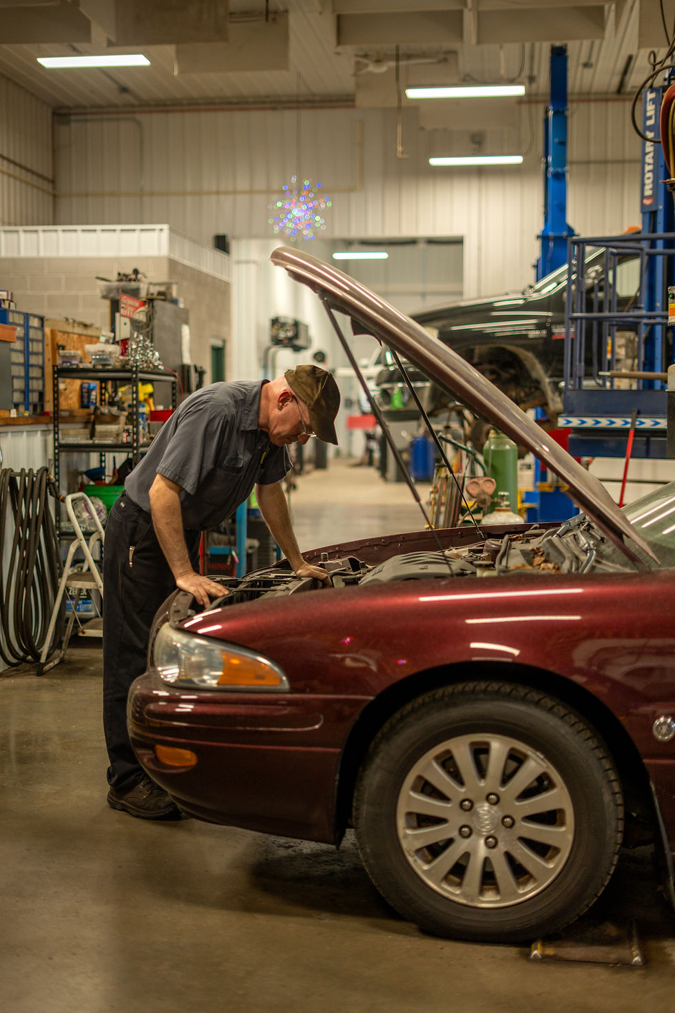 White male looking at engine bay of maroon red buick in shop.