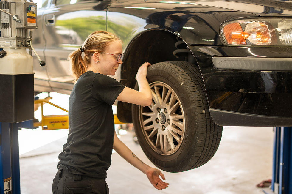 White female with glasses rotating volvo wheel/tire on yellow and blue lift.