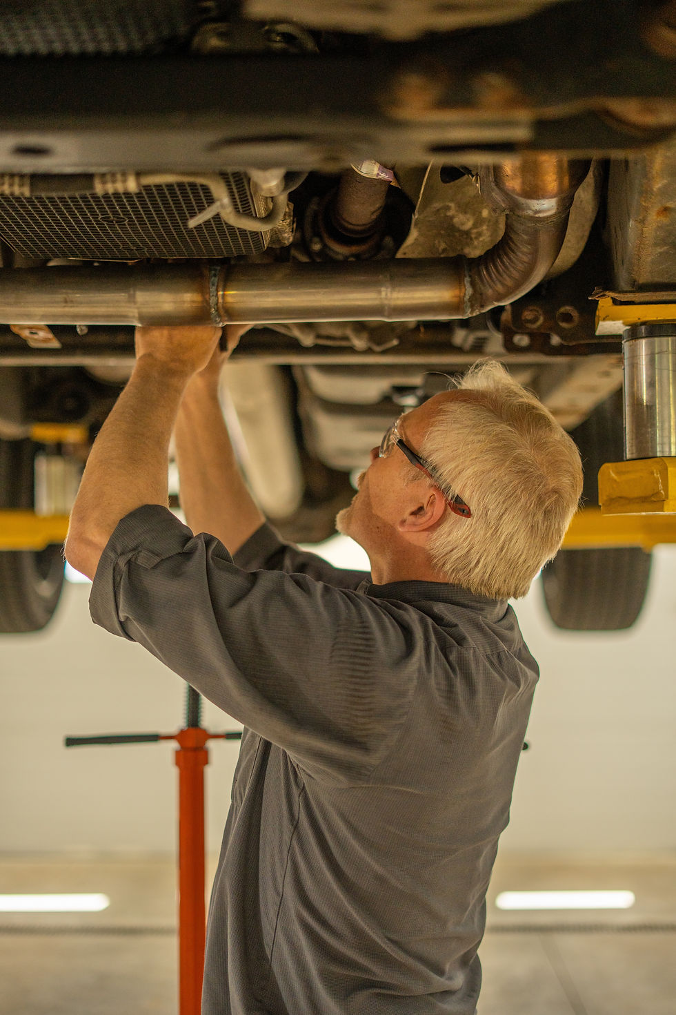 white male fixing driveshaft on underside of vehicle in grey joe's auto uniform