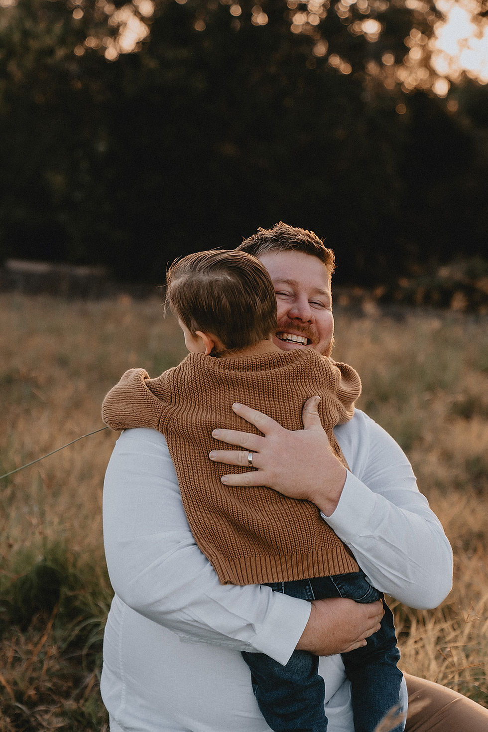 Father and son embrace in a hug in a sunny field with long grass