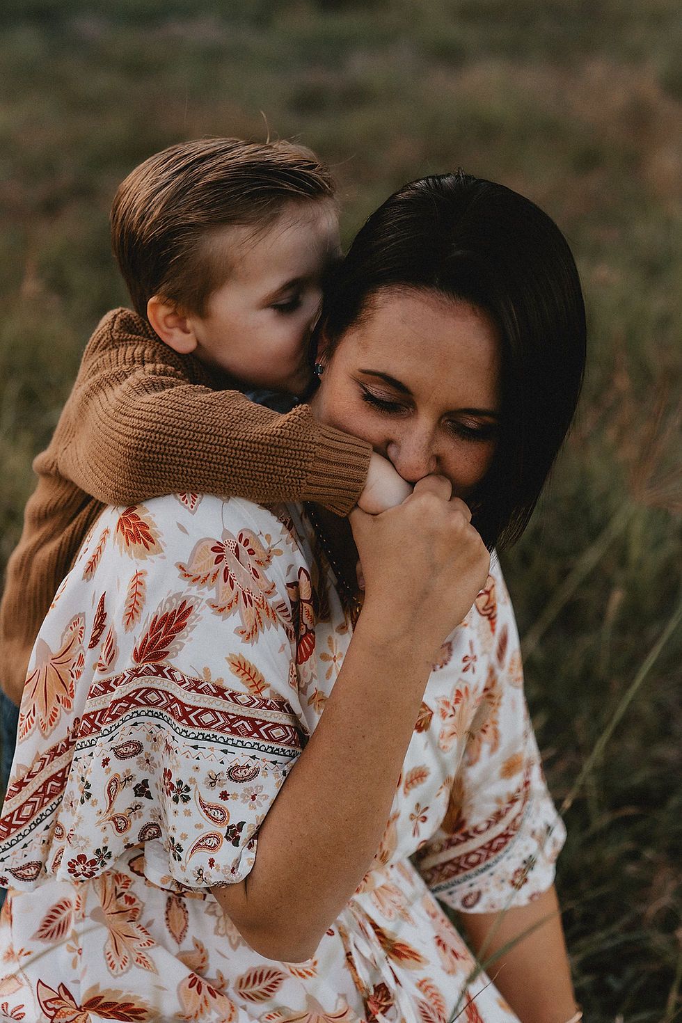 Mother kissing hand of her son as he hugs her from behind