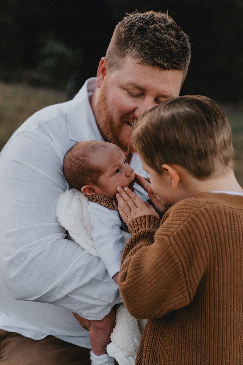 Big brother squeezing cheeks of baby brother being held by dad
