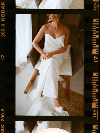 Bride sitting in a chair in her wedding dress during a corfu analog film wedding, lit by window light.