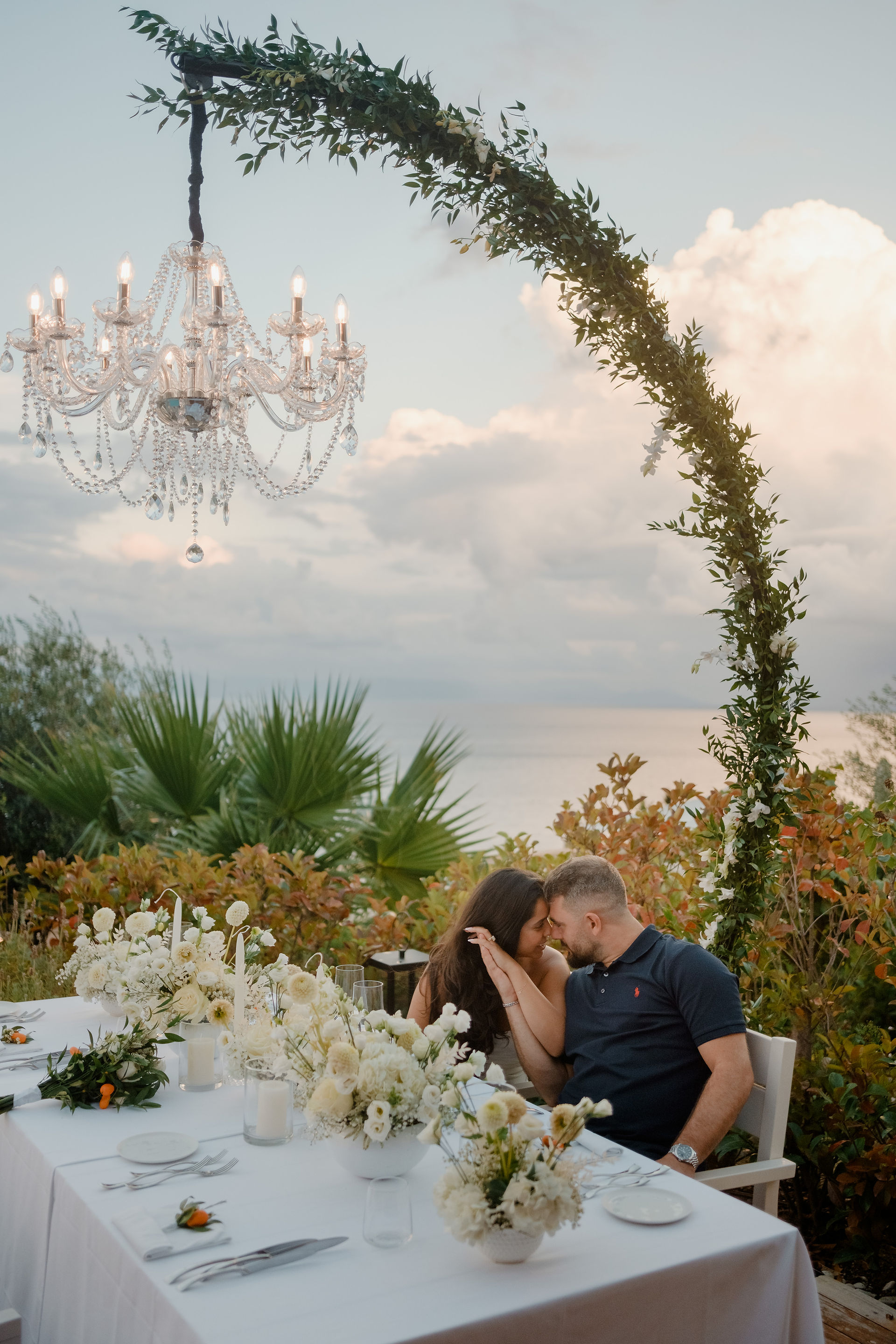 Couple embracing at a floral dinner table under a chandelier during an Angsana Corfu wedding with sea view in Greece.