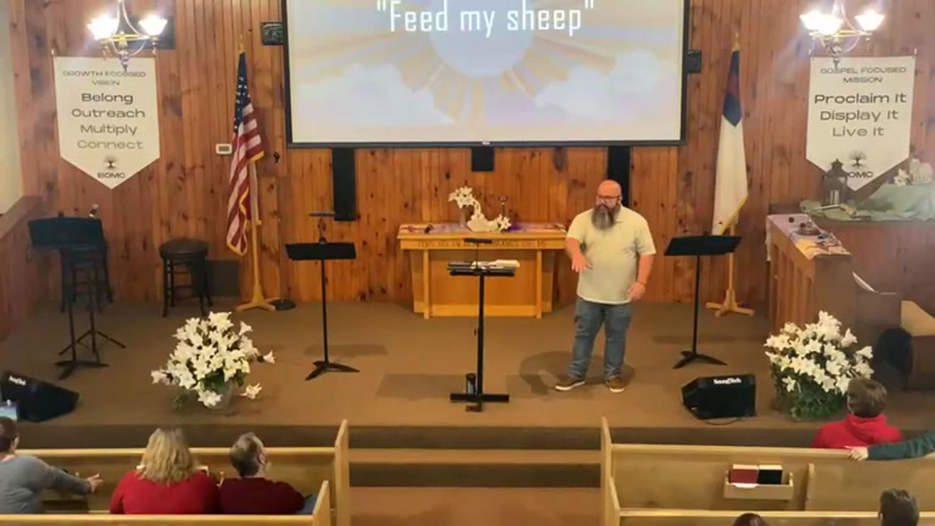 Pastor Ben teaching on a Sunday morning in the BOMC sanctuary, with the BOMC vision and mission banners on either side of the stage