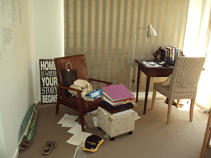 A photo of a messy desk area, with cat sleeping on the floor in the sun