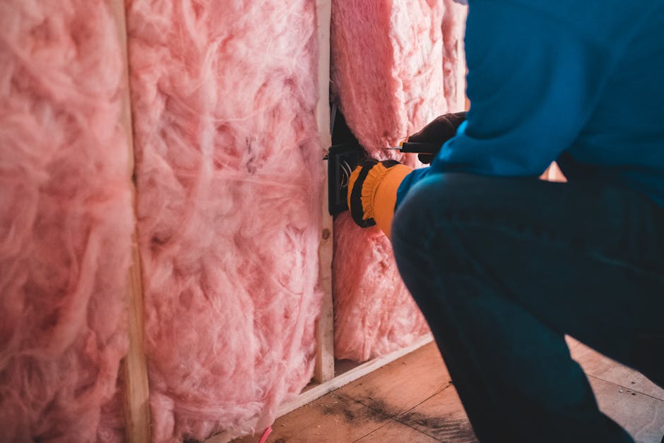 Travailleur installant une isolation en laine de verre rose dans un bâtiment.