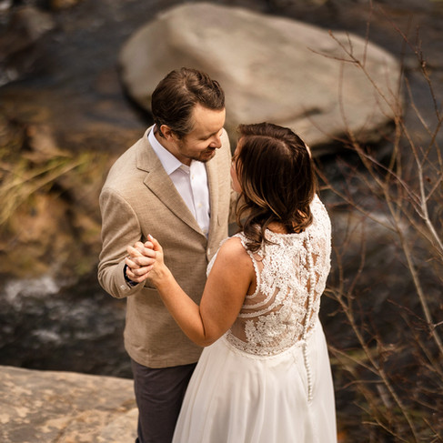 The elopement couple facing each other, holding hands and smiling with Oak Creek in the background.