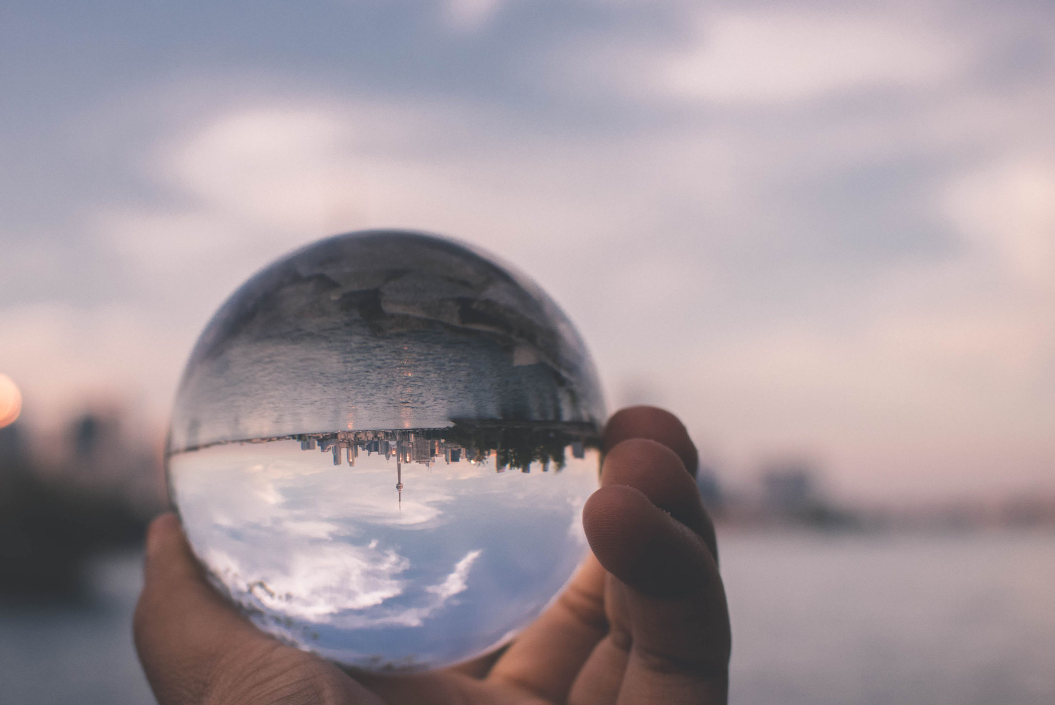 Hand holding a glass ball that reflects city skyline during sunset. Kracht van Ervaring reflection groups