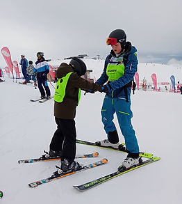 Een begeleider die een deelnemer aan de hand op skis begeleid