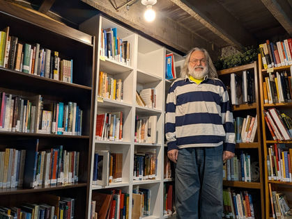 Time Bank member Neil standing in front of a stack of books in the Time Bank library.