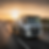 White breakdown recovery truck towing a car on a highway at sunset