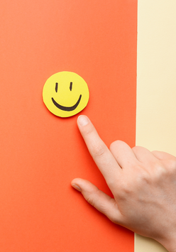 A hand pressing a yellow smiley face button on an orange background.