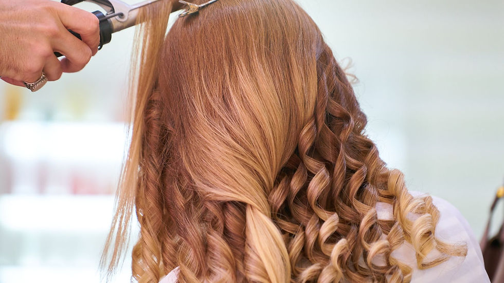Close-up of a stylist curling blonde hair into glamorous curls at a salon.