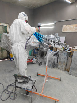 Spray-applied color progresses across the reflective panel in the finishing booth.