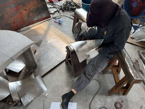 A craftsperson works on the joined stainless-steel sections during fabrication.