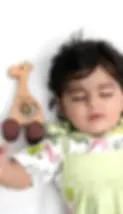 A baby from India rests peacefully beside a wooden rattle in the shape of a giraffe, handc