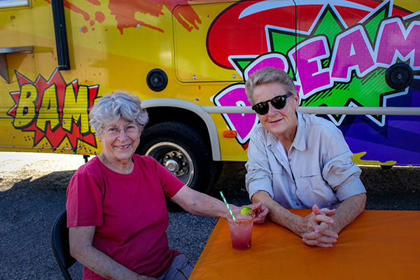 Two women smiling by a colorful food truck at an event
