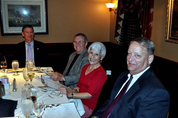 Four people smiling at a dinner table in a photo gallery