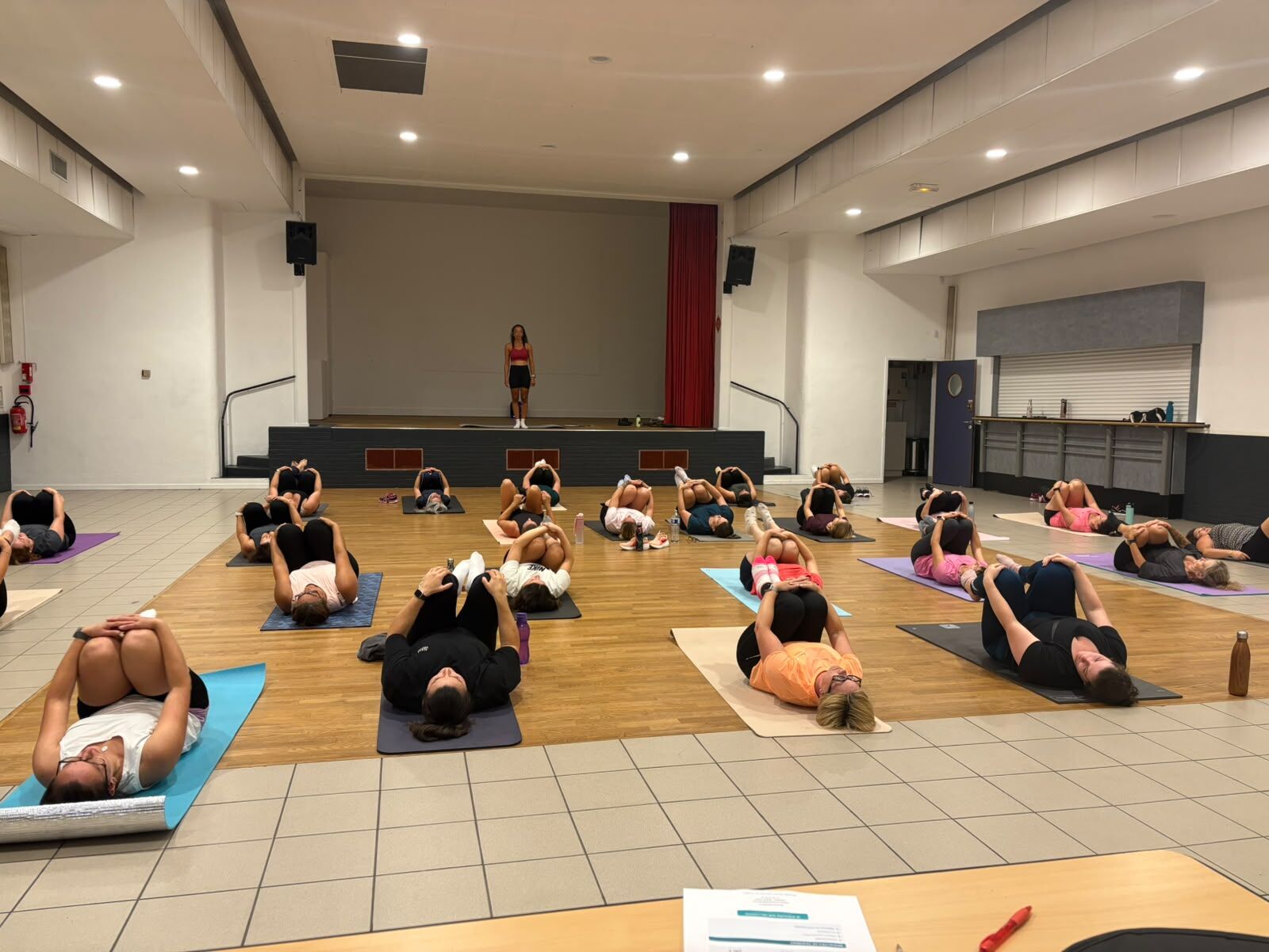 Cours de Pilates guidé depuis la scène devant un grand groupe allongé