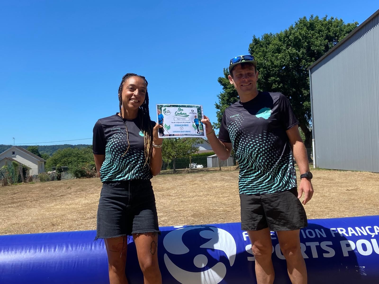 Isabelle et Robin, en tenue Sport Totem, reçoivent un bon cadeau devant l'arche de la Fédération Française Sports pour Tous