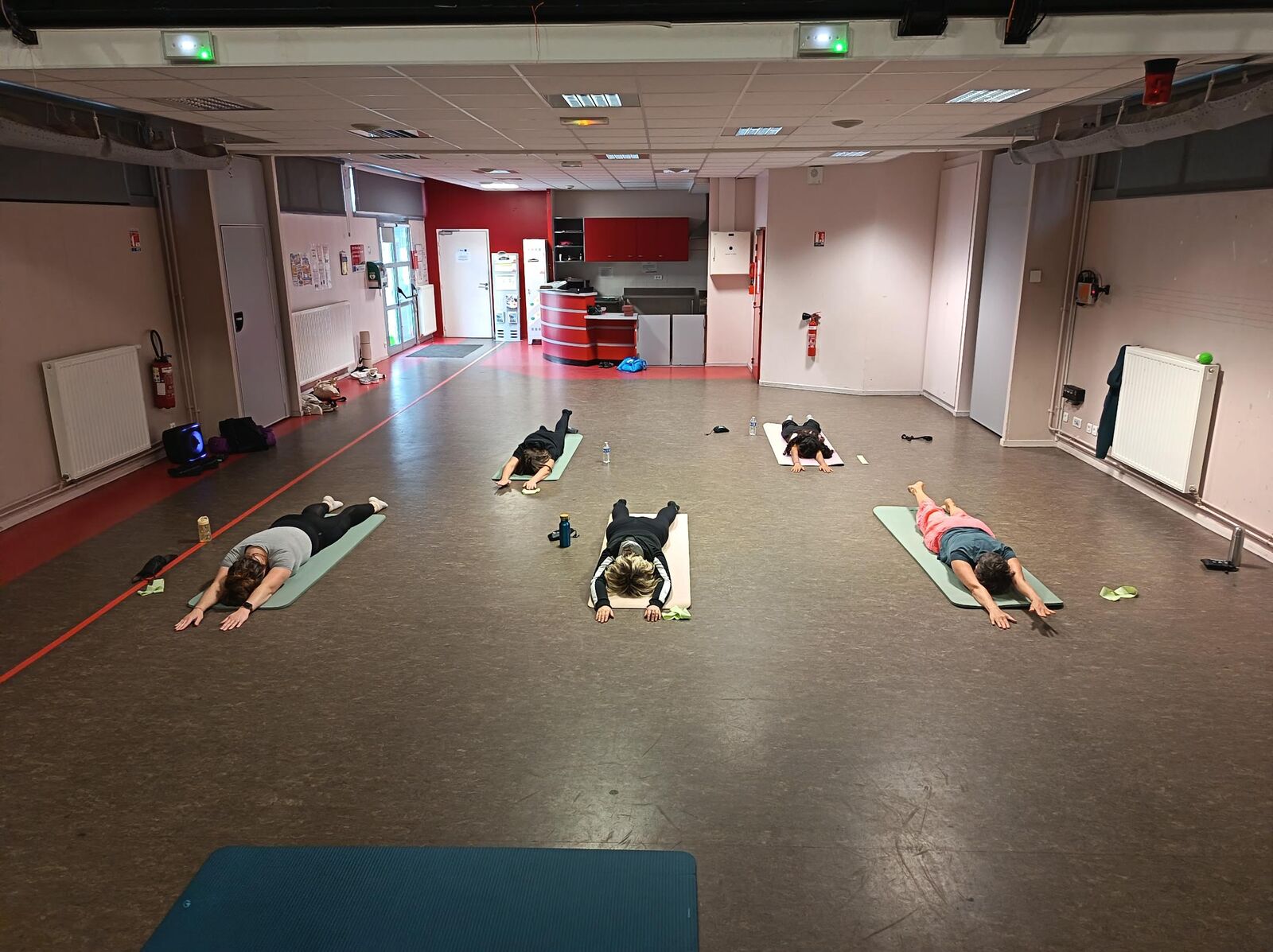 Cours de Pilates dans une salle de quartier, participantes allongées vues de dos