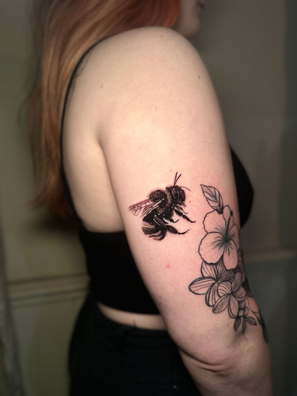 a woman has a tattoo of a bee and flowers on her arm