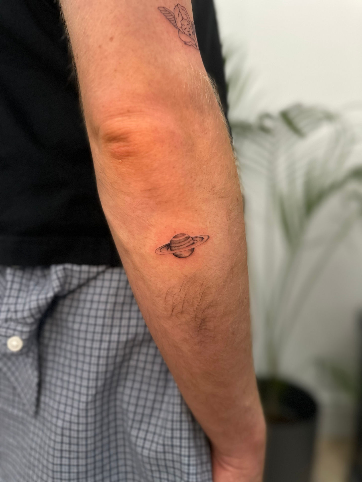 a man has a small tattoo of saturn on his arm