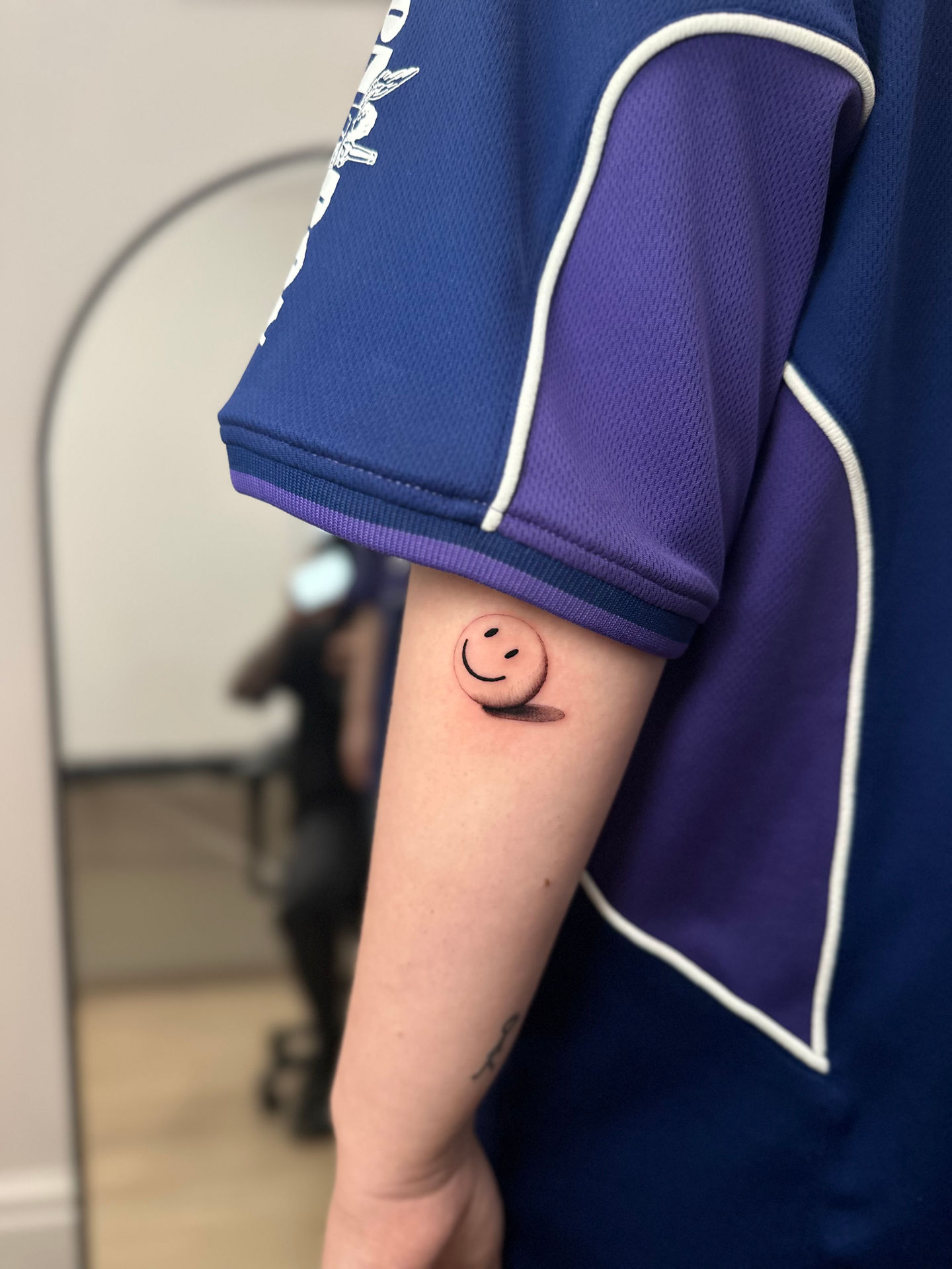 a person with a tattoo of a shaded 3D smiley face on their arm