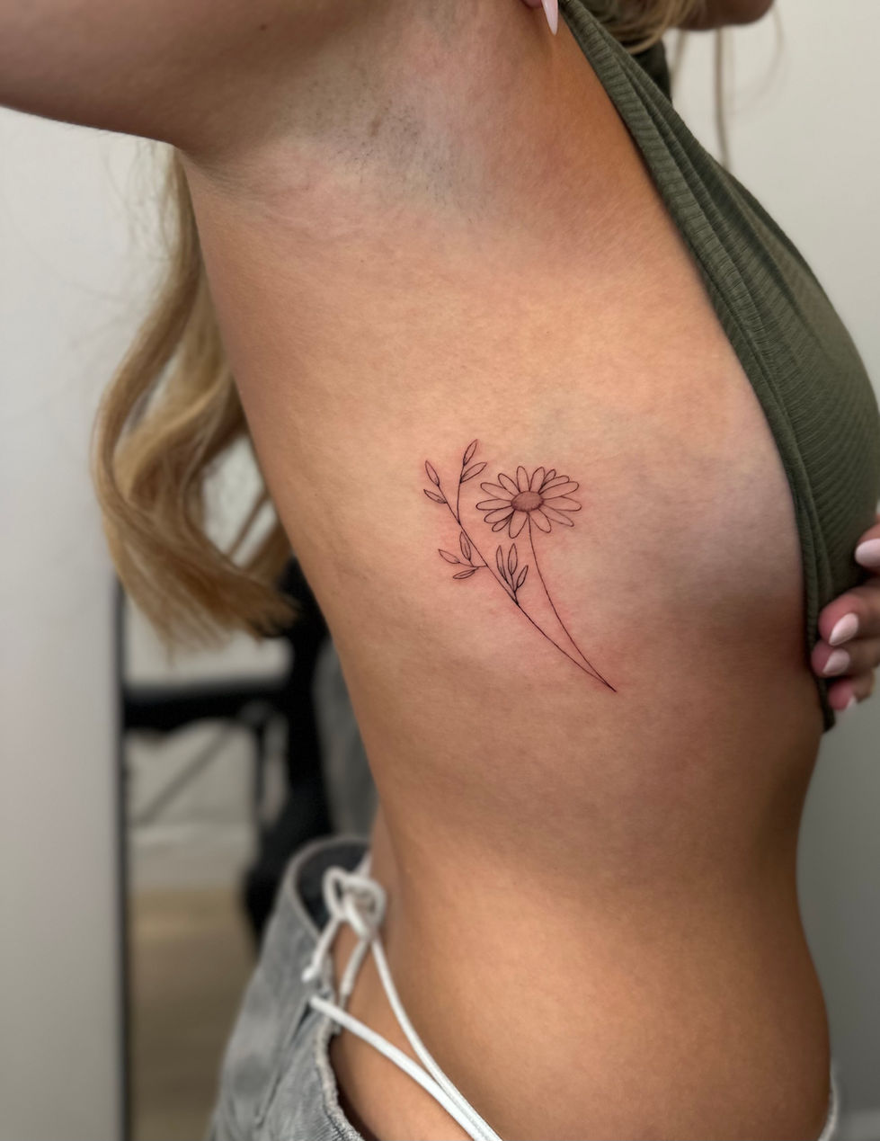 a woman has a tattoo of two daisies on her side