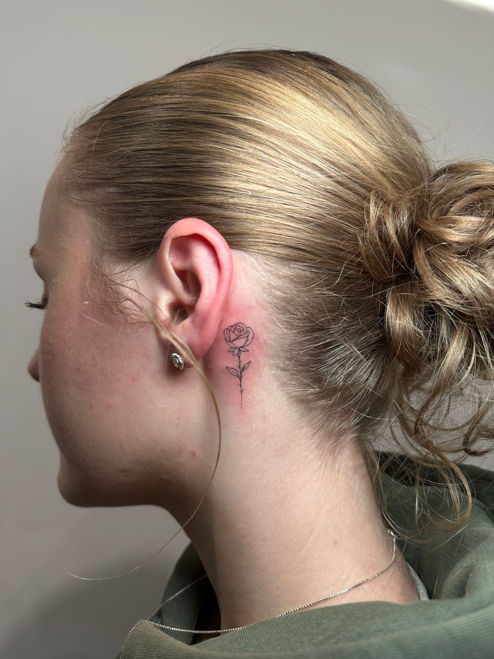a woman has a small tattoo of a rose behind her ear