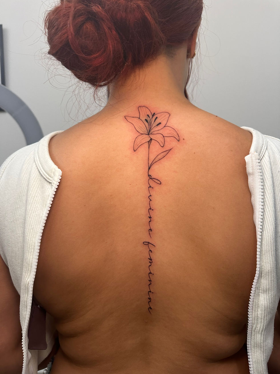 A woman has a fineline floral back tattoo that says divine feminine