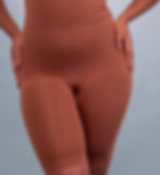Black curvy lady wearing brown skin-matching shapewear shorts holding their hips. Background is gray and smooth, creating a calm, neutral setting.