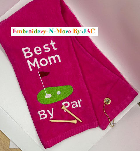 Hot Pink tri-fold golf towel with hook. Embroidered with Best Mom By Par. embroidery is white and there is a golf green with a golf ball, hole and flag.