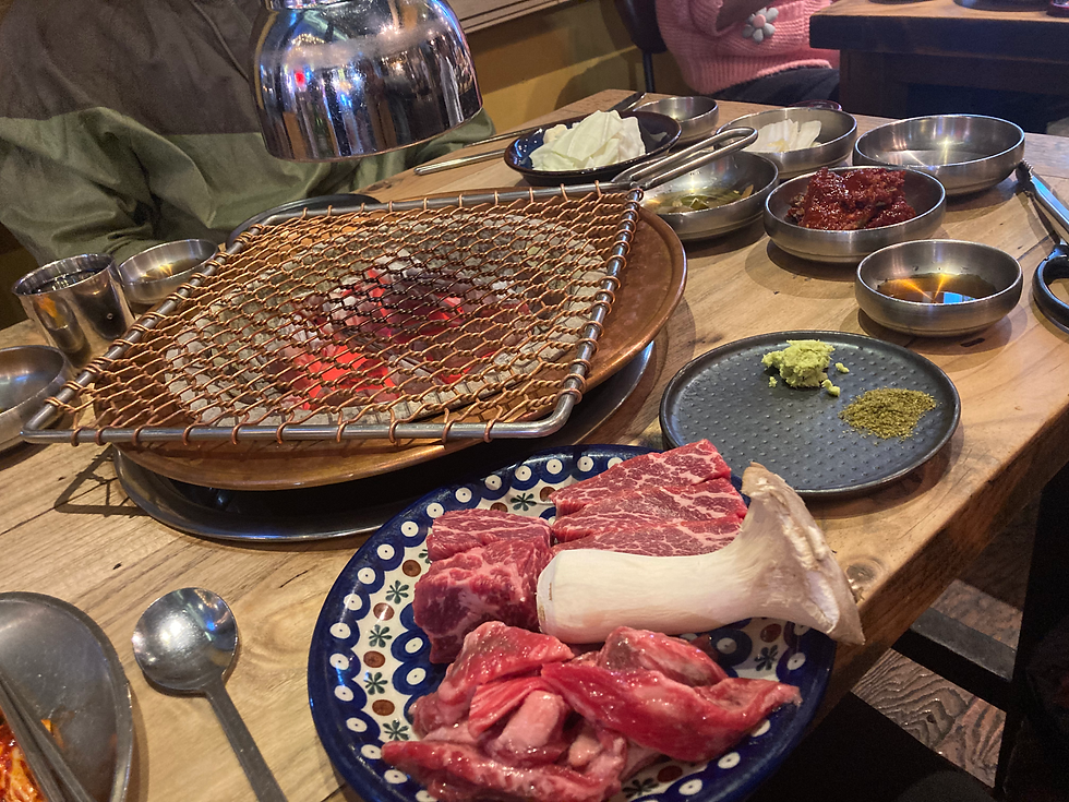 Set up of a Korean BBQ with a grill, raw beef and oyster mushroom with a selection of side dishes.