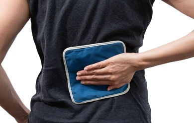 Person applying heat pad to their back. When should you use heat vs. cold for back pain? Discover expert advice from chiropractic doctors at Thomas Back and Body.