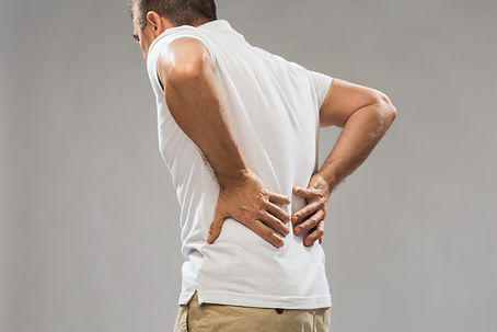 Man in white shirt holding lower back in discomfort, beige pants, against a gray background, indicating back pain. Discover how a Georgetown chiropractor can help end your weekend back pain today.