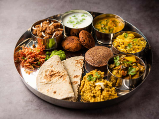 A colorful Indian thali with non-curry, rice, roti, pickles, and salad on a silver plate on a gray background.