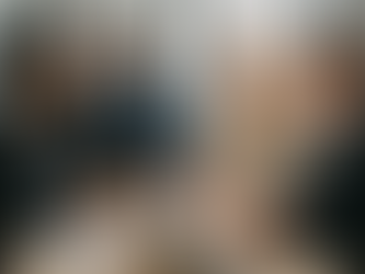 A professional business photograph showing two diverse executive teams engaged in collaborative discussion around a modern conference table with laptops and strategic documents visible.