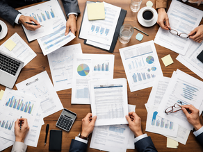 A boardroom table viewed from above — papers and reports spread across it, suggesting a review-heavy environment.