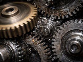 A close-up of interlocking gears of different sizes that are misaligned — one turning freely while others are jammed — representing an operating model that can't keep pace with organizational demands.