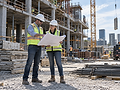Two people in safety vests reviewing plans at a construction site