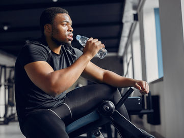 A fit man looking off to the side, drinking a bottle of water